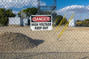 A power substation behind a fence with a "Danger High Volage Keep out" sign.