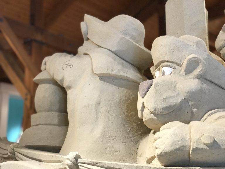 A sand sculpture of bears on a boat wearing sailing uniforms inside of Cuffy’s in West Dennis, Massachusetts. One bear’s face is visible, looking out into the distance.