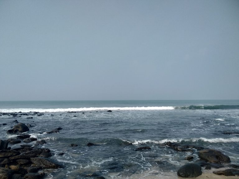 A serene ocean view from a rocky shore, showcasing the beauty of the blue sky, blue ocean, and white waves.