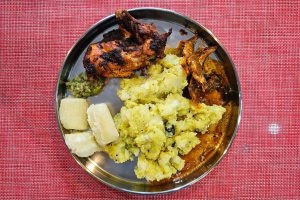 A plate of kachil puzhukku (yam) and boiled tapioca served with sardine chilly curry, green chilly chutney, and grilled chicken. 