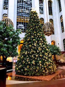 Tall Christmas Tree decorated with gold painted baubles, decorations, a large lit star on top. Surrounded by large ball shaped decorations and two glossy green trees. Ritz-Carlton Hotel, Atlanta, Georgia, USA.