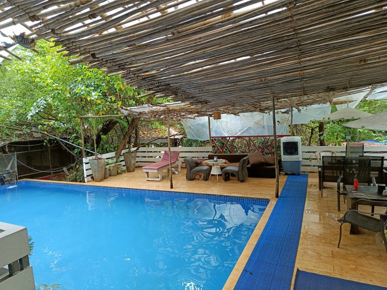 Swimming Pool in a backyard with some chairs, table and a cooler.