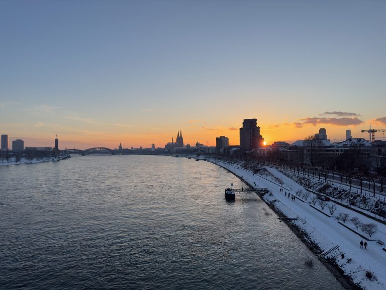 Rhine river and its snowy promenade with the Cologne Cathedral at sunset as viewed from Zoobrücke bridge.