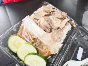 A plastic container filled with a delicious meal of meat, rice, and fresh cucumbers.