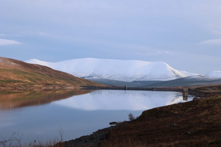 Snow covered Ben Wyvis and Glascarnoch Dam reflecting into Loch Glascarnoch Scottish Highlands