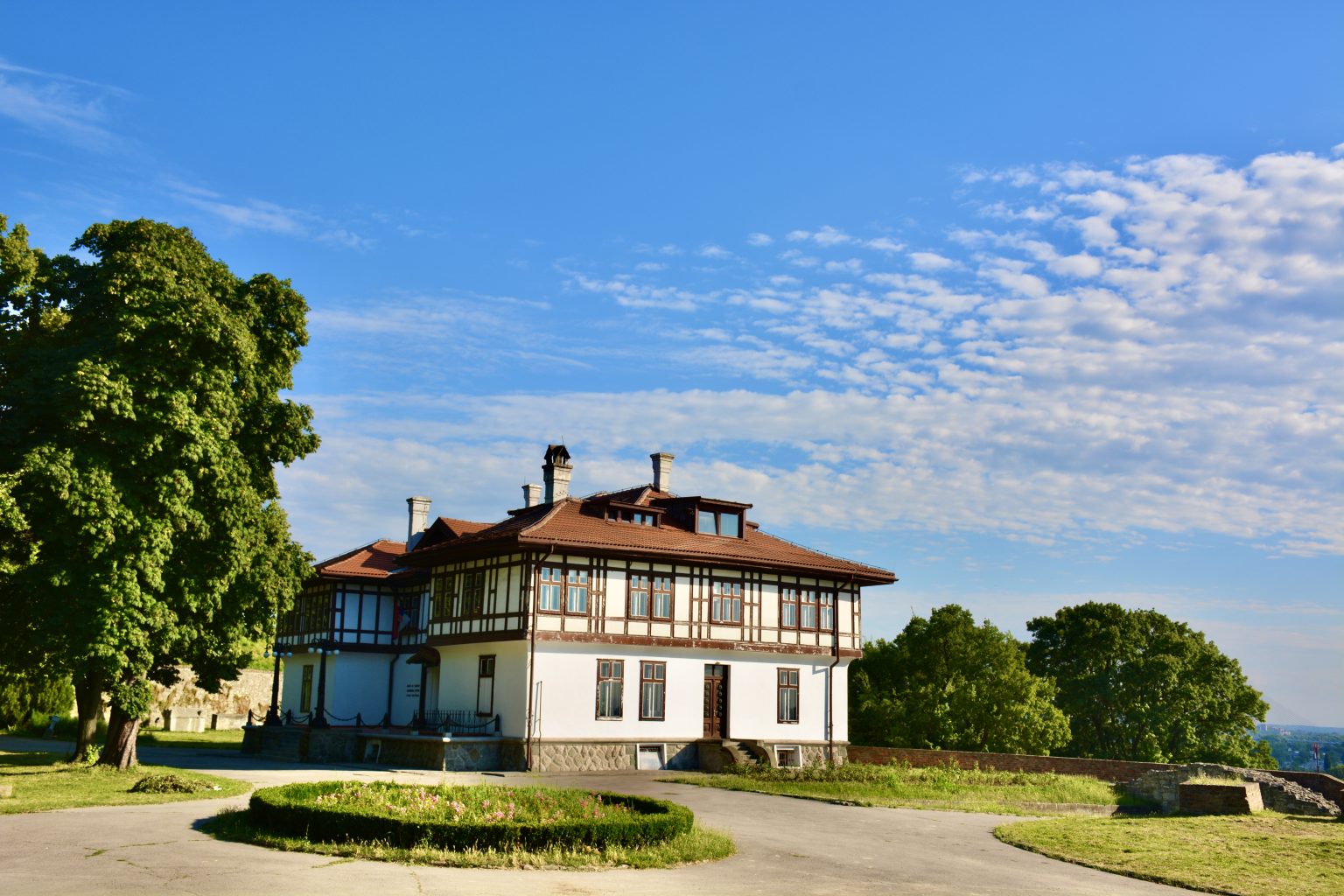 Institute for the Protection of Cultural Monuments in Belgrade fortress, Serbia, is a white 3-story building with a spacious yard and blue sky.