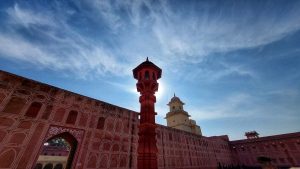 View larger photo: View from part of Jaipur's City Palace in India, with the sun sparkling off an ornate tower in the foreground. The sky is blue and with some white clouds. The color of the palace is pink in keeping with the city's color scheme.