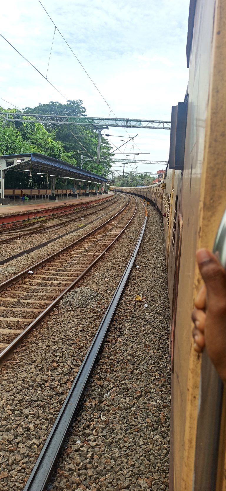 Looking down along a train at train tracks with a station to the left where people wait for the trains.