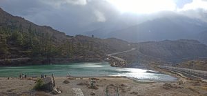 Sun is shining on the valley and river with people on the banks. Also, a road going across the mountains.