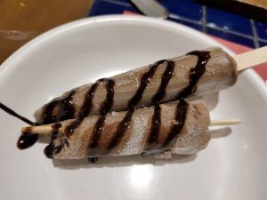 Two ice cream pops with chocolate syrup on a plate.