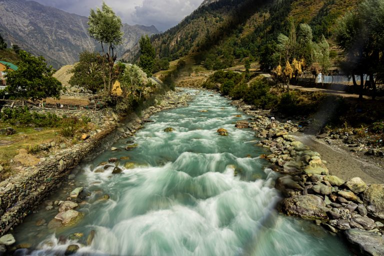 A stream runs through a valley in the mountains. Stones line the banks.