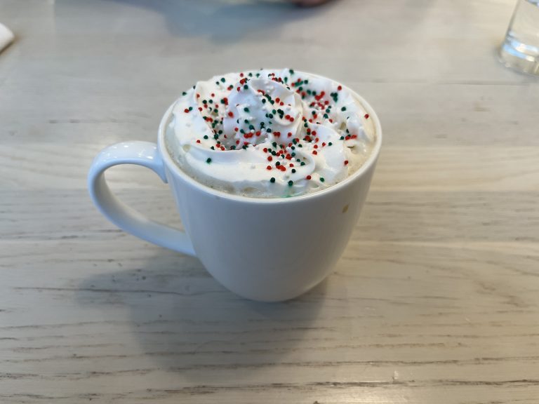 Drink in a mug with whipped cream and sprinkles on top.