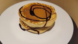 Homemade Pancakes with chocolate syrup served on a white ceramic plate.