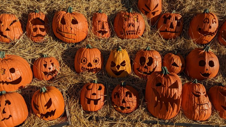 A hay stack filled with decorated jack o’ lantern pumpkins.