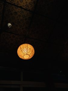 Orange color decorative paper lantern hanging on the ceiling. along side a security camera.