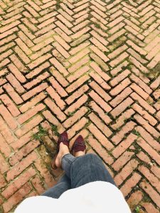 A person's legs and feet on a brick path in a herringbone design