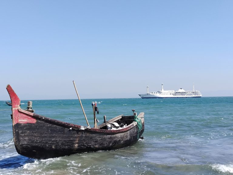 A fish boat stand front of cruise ship in sea.