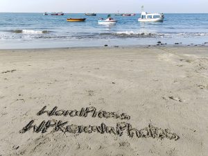 Writing down WordPress and WPKeralaPhotos in sand of Saint Martin Island with boats in the water in front of the beach