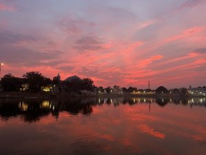 Lake during evening with illuminated buildings on the shore and colorful sky with its reflections in the water. 
