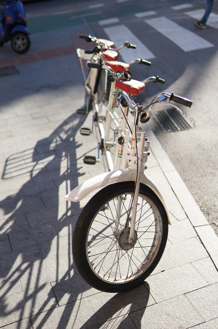 White four-person tandem bycicle parked in the street.