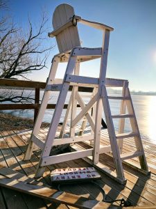 Lifeguard chair sitting on a beach dock at sunrise with a signing laying next to it describing "No Entry Without Lifeguard" (Fish Lake, YMCA Camp Duncan, Ingleside, Illinois)