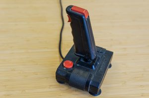 Old black and red joystick type video game controller sitting on a table