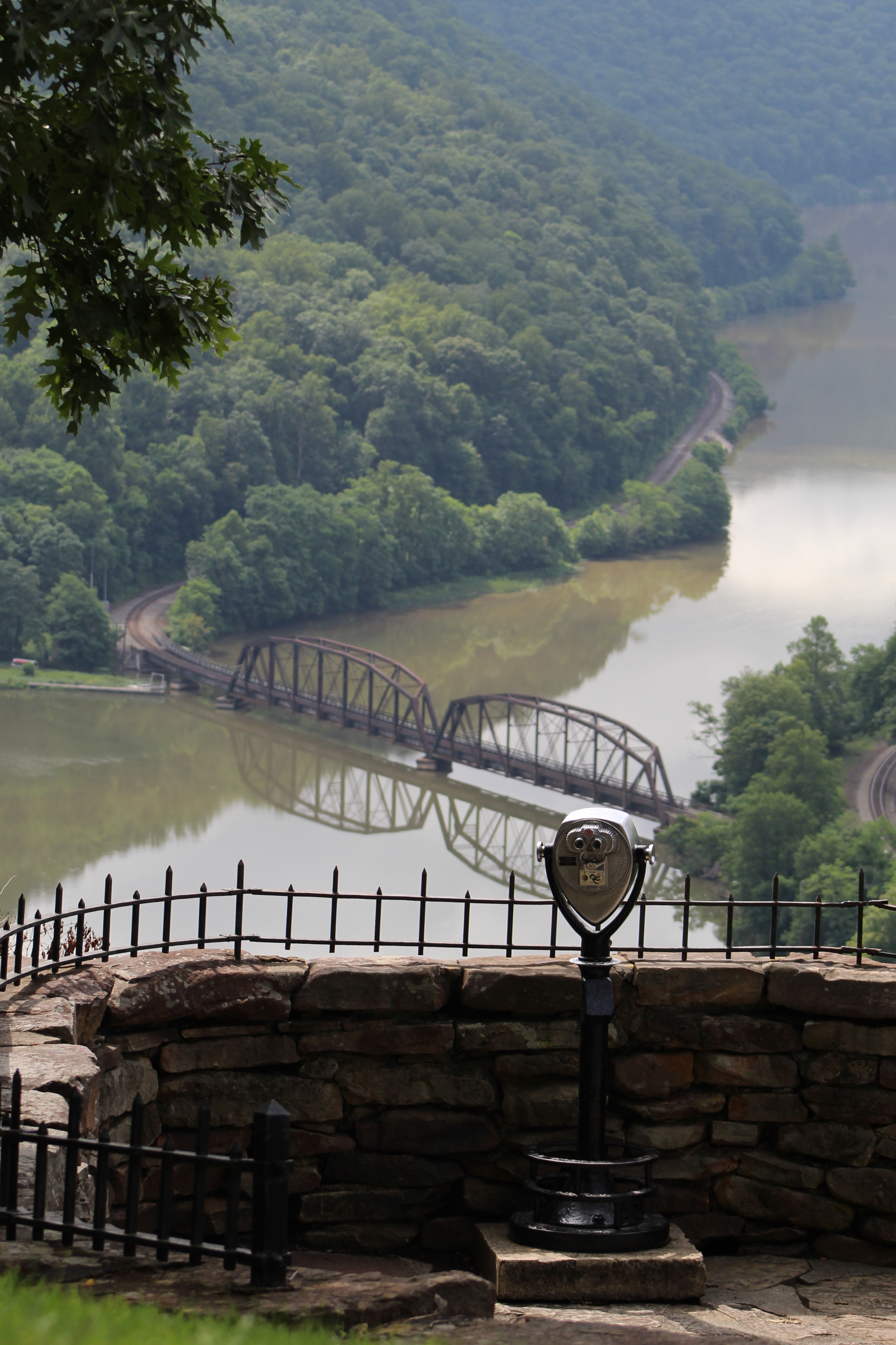 Hawks Nest State Park overlook, New River Gorge, West Virginia, with binoculars in the foreground overlooking a river with a train bridge and hills in the background.