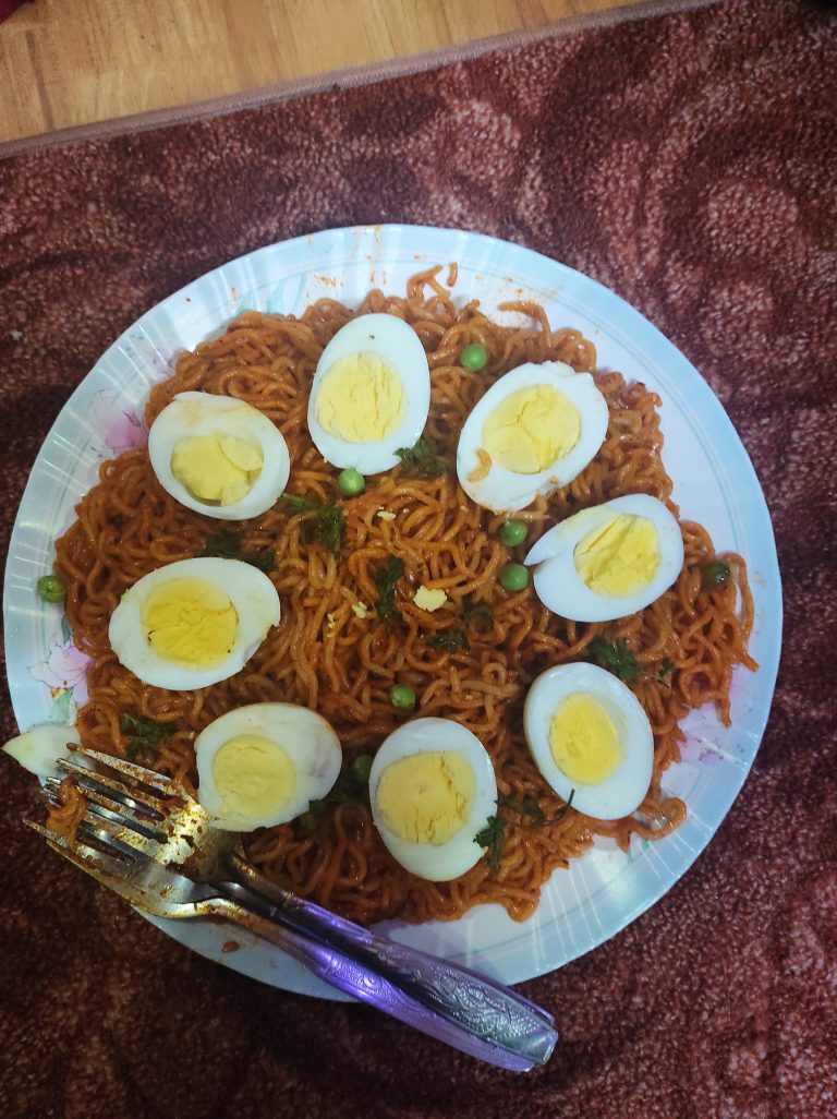 A plate containing boiled half eggs alongside spicy noodles, accompanied by a spoon.