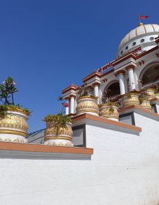 A white building with gold and red trim against a bright blue sky
