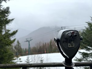 Coin operated binoculars on a deck at a lookout point on Loon Mountain in Lincoln, New Hampshire. It’s a rainy day with heavy clouds concealing the mountains in the distance.
