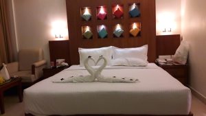 Hotel room with towels shaped like swans making a heart on the bed.