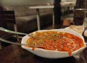 Paneer Kadai dish served on table with two submerged utensils and a partial glass of water behind it.