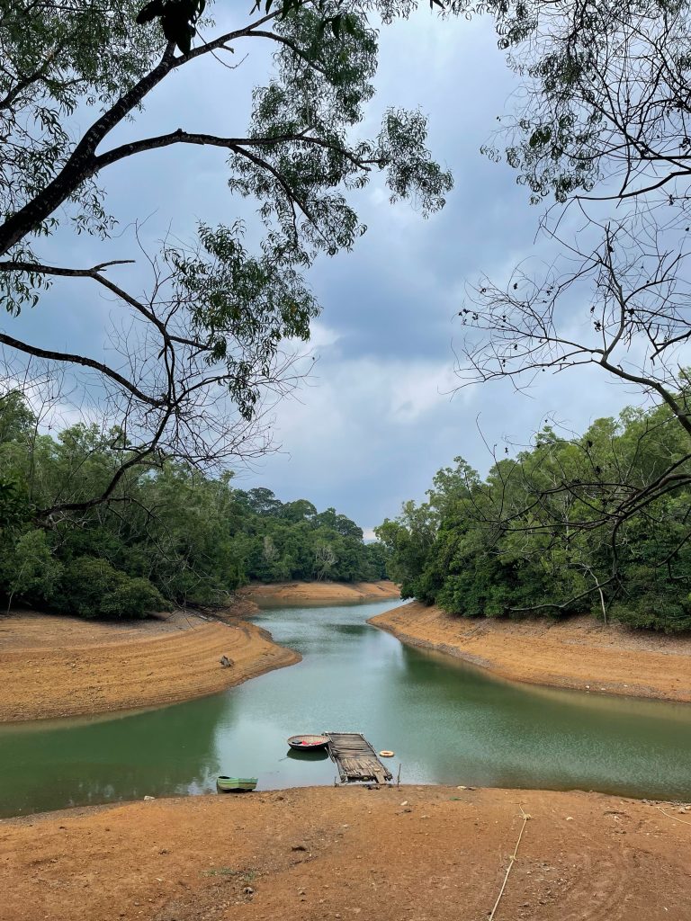 Brown dirt banks rise up from a river that goes off in three directions. There is a small pier and boat on the nearest shore.