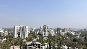 A view of Pune City from up high. White highrises above green palm trees.

