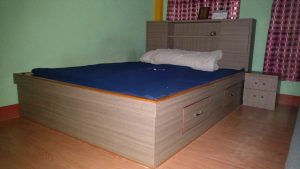 A bed with a blue bed cover and a white blanket is in the room, and a small bed box is on the side of the bed.