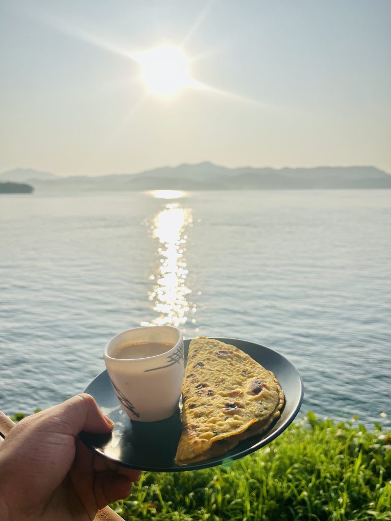 A hand holding a black plate containing tea and Paratha on Mountain View in the Morning.