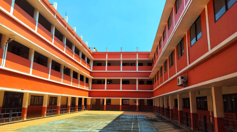 Counrtyard of a college building, a tennis cout painted on the surface. Clear blue sky above.