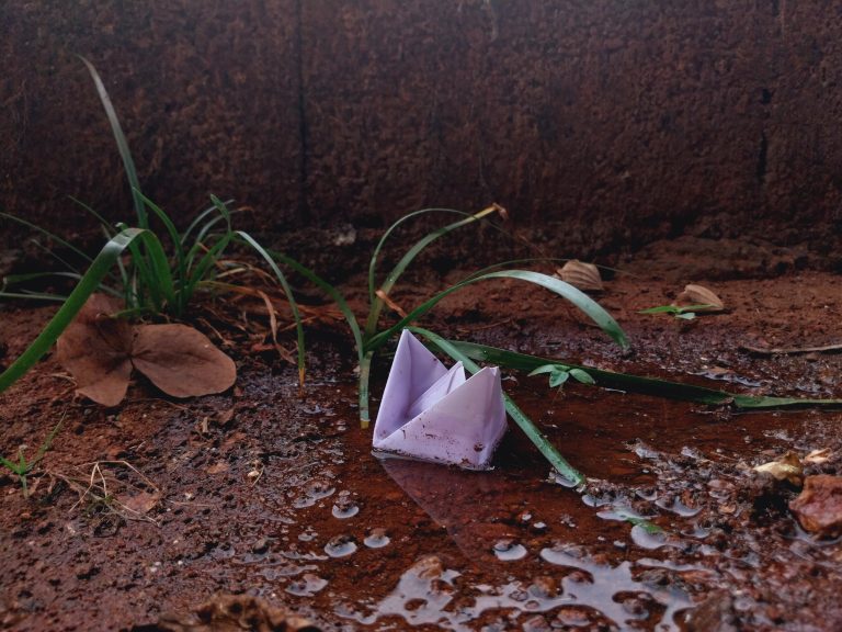 Memories bring back your childhood, A paper boat floating in a puddle of water after the rain.