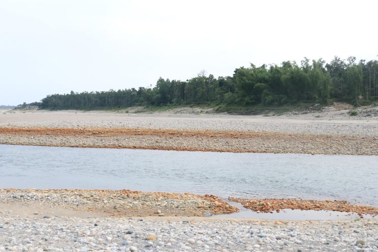 A river flows between rocky banks with trees in the background