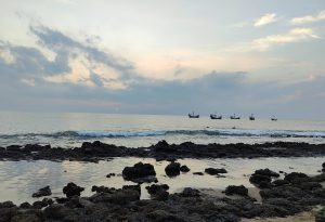 Sunset view from a rocky beach with boats sailing in the sea. Saint Martin Sea.
