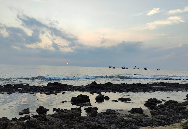 Sunset view from a rocky beach with boats sailing in the sea. Saint Martin Sea.