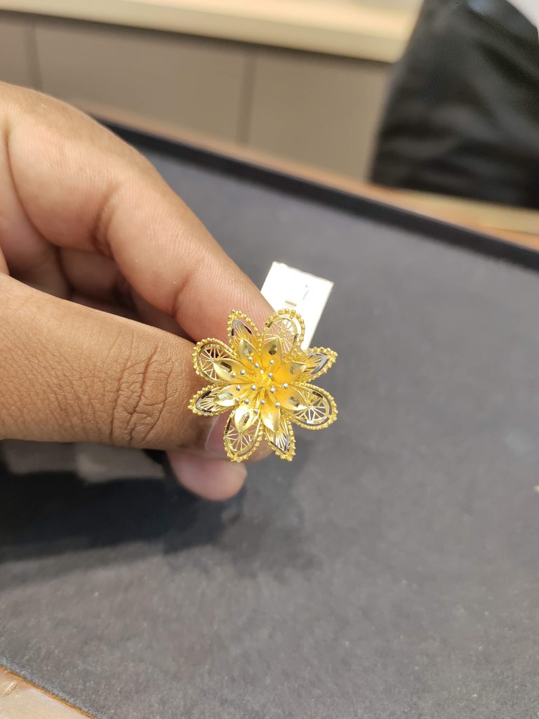 A person is holding a gold finger ring with a flower on it.