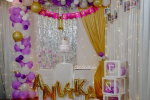 Birthday stage decorated with balloons, photos, and cake in the centre, 