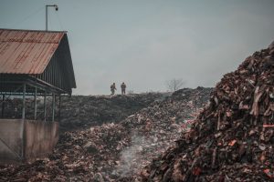 Two people stand atop a large landfill with heaps of waste, highlighting environmental challenges and pollution.