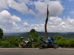 Two motorcycles in the mountains with a beautiful blue sky filled with clouds.

