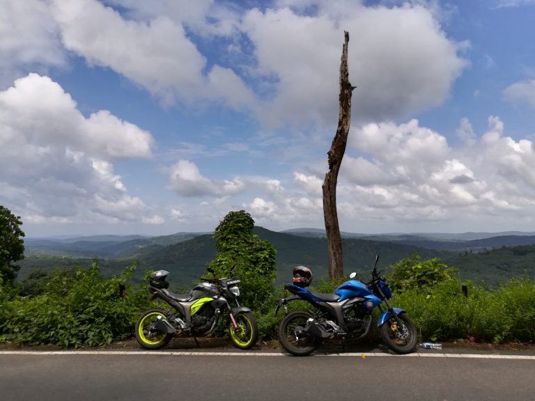 Two motorcycles in the mountains with a beautiful blue sky filled with clouds.