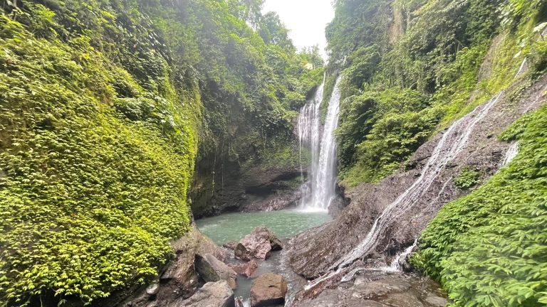 Two waterfalls flow into a pool at the bottom of a ravine