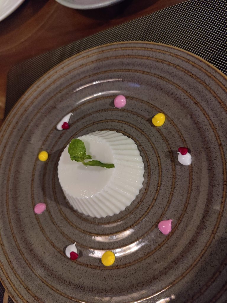 Coconut pudding garnished with mint leaf and served on a ceramic plate.