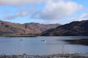 Sailing boats and a fishing boat on Lochcarron on a still clear day in the Scottish Highlands.
