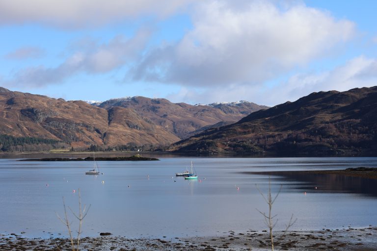 Sailing boats and a fishing boat on Lochcarron on a still clear day in the Scottish Highlands.